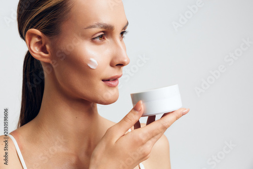 Photos Closeup of a woman applying moisturizer from a jar, soft light highlights flawless skin, calm expression, and a skincare routine moment, natural colors, clean background, gentle touch