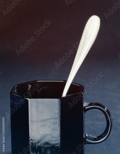 Canvas Print Glossy black ceramic mug with a silver spoon standing inside against a dark background
