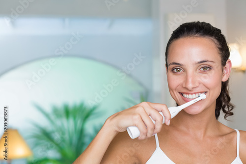 Foto 20s-woman standing at bathroom vanity brushing teeth with electric toothbrush in