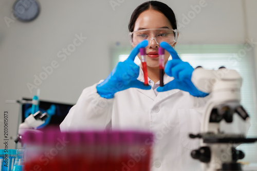 Tableau sur toile Female scientist wearing safety glasses and blue gloves, holding and examining t