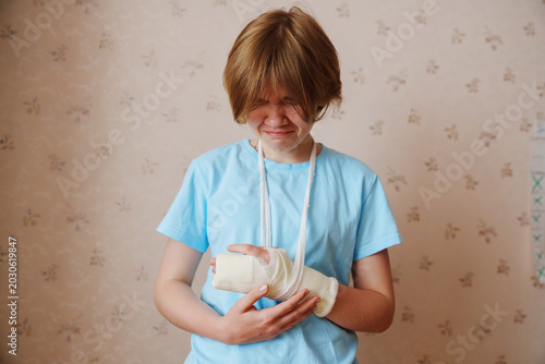 Person wincing in pain, holding injured arm in cast and sling