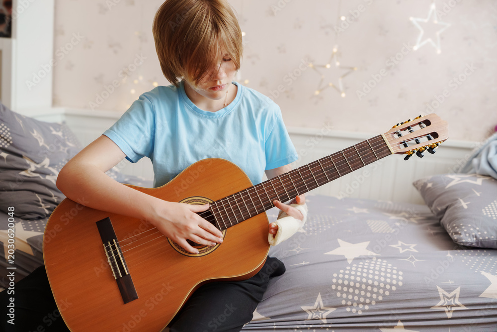 Fototapeta premium Pensive Teen Musician Analyzing Guitar Fretboard with Injured Hand
