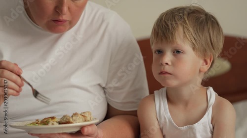Mother feeding her little son breakfast in bed