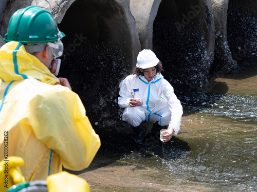 Фотография Environmental engineers in chemical protective suits are collecting samples of contaminated water, ecologically and industrially, from nearby areas for testing