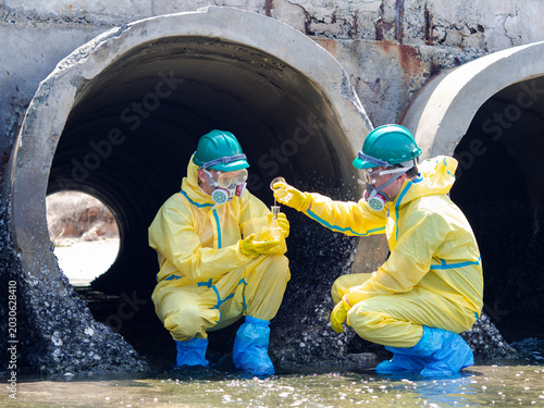 Konstfotografi Environmental engineers in chemical protective suits are collecting samples of contaminated water, ecologically and industrially, from nearby areas for testing