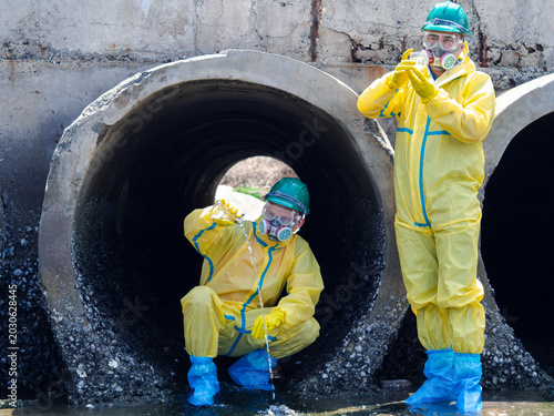 Konstfotografi Environmental engineers in chemical protective suits are collecting samples of contaminated water, ecologically and industrially, from nearby areas for testing