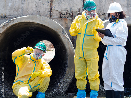 Tableau sur toile Environmental engineers in chemical protective suits are collecting samples of contaminated water, ecologically and industrially, from nearby areas for testing