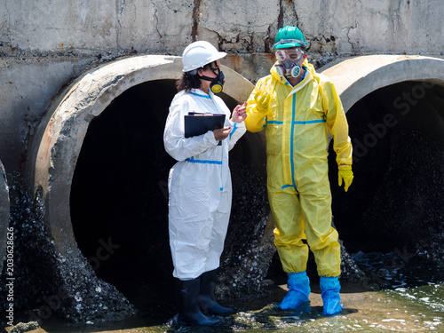 Tableau sur toile Environmental engineers in chemical protective suits are collecting samples of contaminated water, ecologically and industrially, from nearby areas for testing