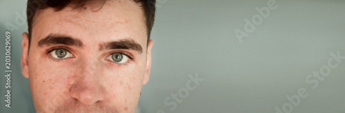 Close-up portrait of a young man with freckles and green eyes. Panoramic shot of a male face with clear skin texture and expressive look on a neutral background. Banner with copy space