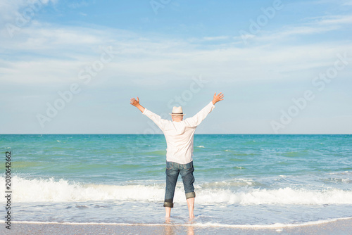 Rear view of senior man with arms raised enjoying freedom on beach during summer vacation