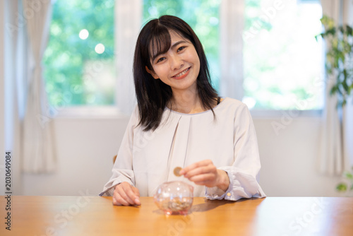 Foto Asian woman smiling while putting coins into piggy bank