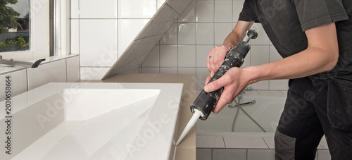 Interior of a modern bathroom in an apartment. Man kitting the bath tub with a kitting pistol. Plumber