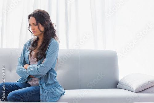 Canvas Print Female sitting left on light gray sofa, in denim, crossing arms, sheer curtains