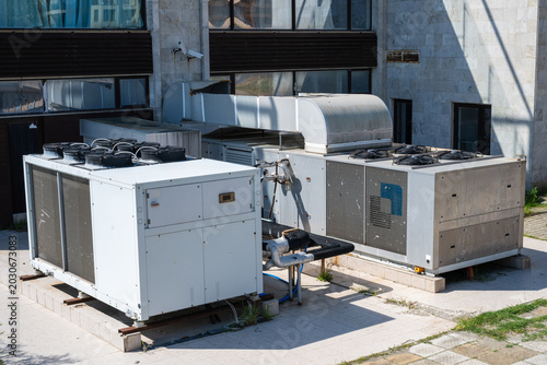 large commercial hvac units and metal ductwork sit on a concrete pad outside a building.