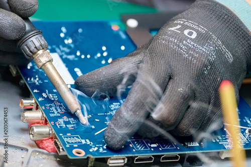 Photos Expert technician solders components on a blue circuit board during an electroni