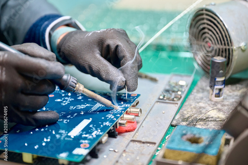 Skilled technician soldering electronic components on a circuit board in a workshop