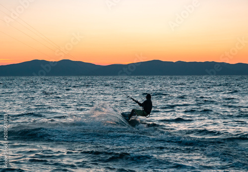 Kitesurfer rides ocean waves under a beautiful gradient sunset sky and distant mountains