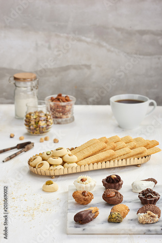 elegant Eid holiday sweets assortment, featuring decorated petits fours, traditional butter biscuits, and Ghorayeba cookies with pistachios, beautifully styled on marble and golden trays with coffee.