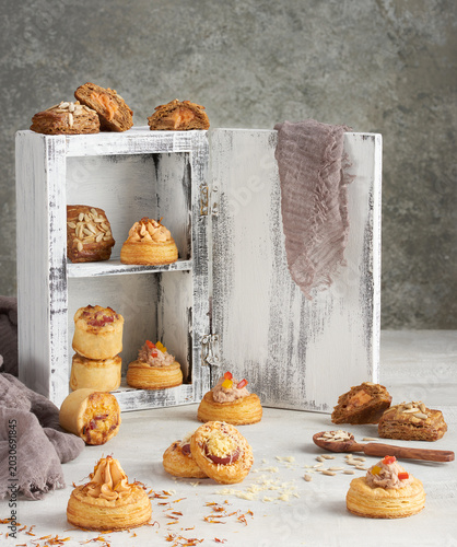 gourmet savory pastry assortment, including puff pastry canapes, vol-au-vents filled with cream and tuna, and mini quiches, creatively displayed in and around a rustic, weathered white wooden cabinet 