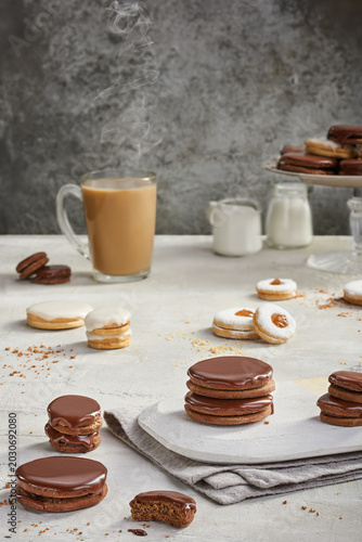 chocolate-dipped Sablé cookies, elegantly stacked on a white board with a steaming mug of milk tea
