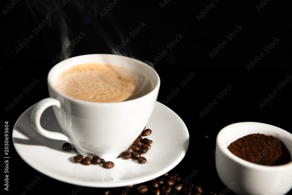 Obraz premium Premium dark roast arabica coffee beans with cozy cup of warm steaming coffee and sugar on dark background with copy space