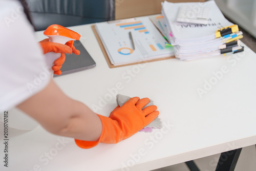 Foto Person in orange gloves cleaning white desk surface with spray