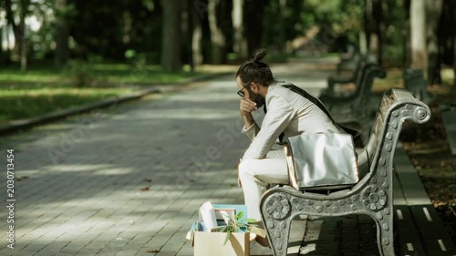 Fired Businessman Sitting On Bench Near Box With Personal Belongings. Dismissed Employee Thinking About Job Loss Crisis. Unemployment 