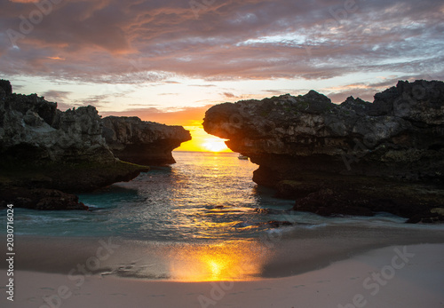 Fotografía A view of the sunset on the beach with orange light penetrating the gaps in the cliffs on Mandorak Beach, Sumba Island, East Nusa Tenggara Province