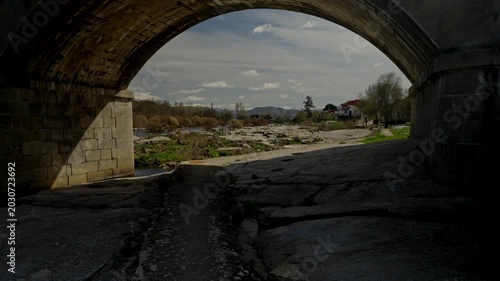 Stone bridge arch framing sunlit river with rocky banks