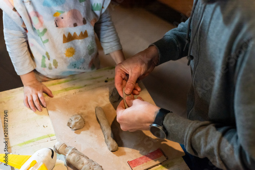 Foto Adult teacher or father hands helping little girl shape clay on pottery wheel in