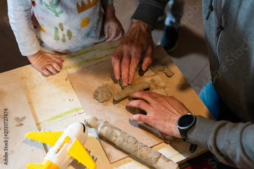 Foto Adult teacher or father hands helping little girl shape clay on pottery wheel in