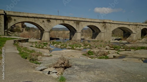 Old stone bridge with multiple arches crossing a low water river featuring ex...