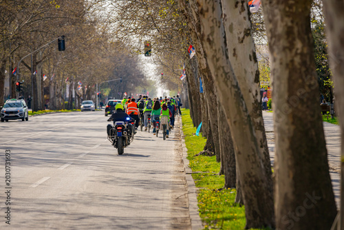 Police officer on motorcycle secures group of cyclists on city road, street, asphalt