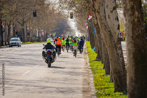 Police officer on motorcycle secures group of cyclists on city road, street, asphalt