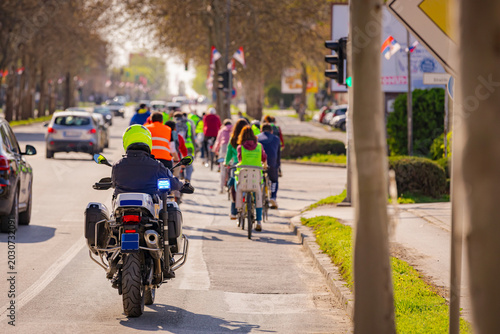 Police officer on motorcycle secures group of cyclists on city road, street, asphalt