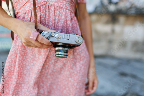young girl with a camera in her hands.  the photographer adjusts the camera. Stylish girl in a pink dress with a film camera in her hands. adventures and travel.