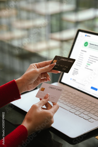 Woman holding credit cards while making a successful online payment on laptop computer, representing e-commerce, digital banking, and secure online shopping at home.