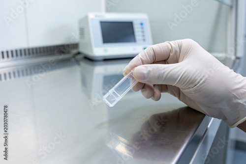 Tableau sur toile Scientist in sterile gloves holds a small transparent sample container in a labo