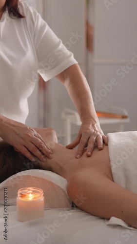 A skilled therapist gently massages a client's neck and shoulders, promoting stress relief and wellness. The warm glow of a candle creates a peaceful, inviting spa ambiance