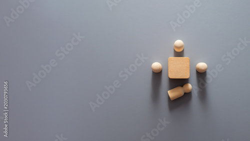 Obraz na płótnie Minimalist wooden peg figures arranged around a central wooden block with one figure lying apart from the group, symbolising employee turnover, workforce reduction, staff resignation, talent loss