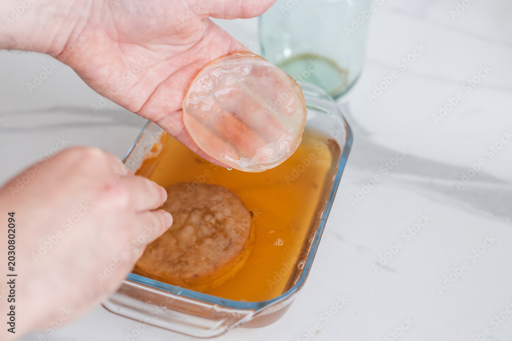 Φωτογραφία Kombucha scoby being lifted from glass dish with amber tea for homemade kombucha