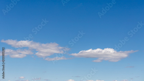 A wide expanse of clear blue sky dotted with soft white clouds, creating a pe...