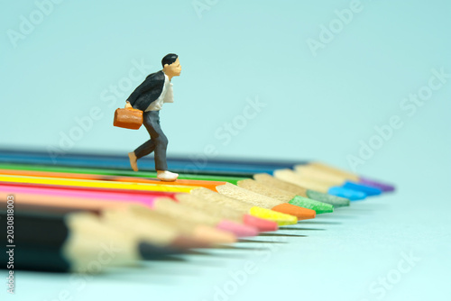 Miniature tiny people toys photography. A boy pupil student running above colorful pencil color. Isolated on blue background