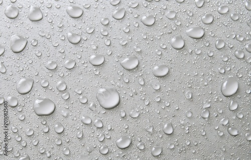 Silver surface covered in numerous water droplets of various sizes, glistening with light