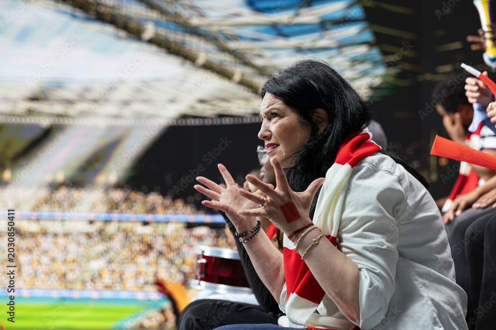 Naklejka premium Frustrated mature woman football fan gesturing with open hands in disbelief during tense soccer match from stadium stands. Dejected supporter showing disappointment, football defeat.