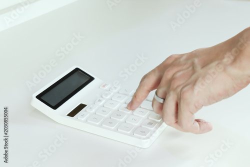 Close-up of a hand pressing a white calculator on a clean desk, representing budgeting, finance, accounting, expense planning, and business calculation in a minimal office setting