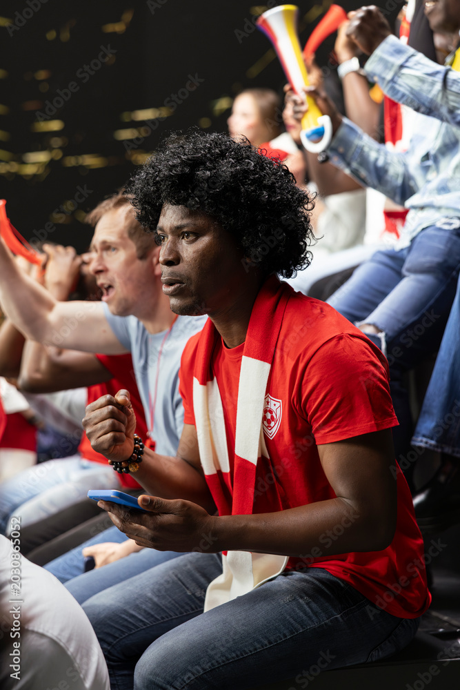 Naklejka premium Football fan checking smartphone during tense match, framed as a close vertical sports image.