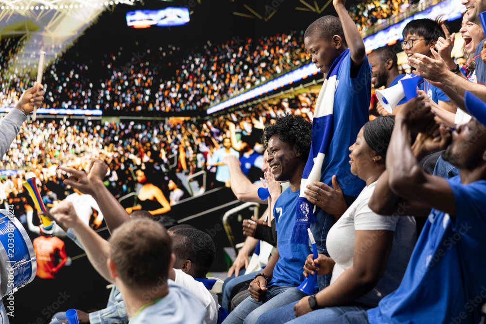 Fototapeta premium Black parents enjoying quality family time at football stadium, cheering for blue team during intense soccer match. Family sharing excitement of live sports with child fan, role model.