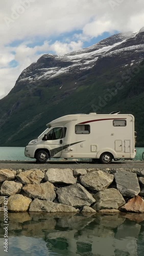 Motorhome parked by mountain lake in dramatic alpine landscape, vertical travel scene.