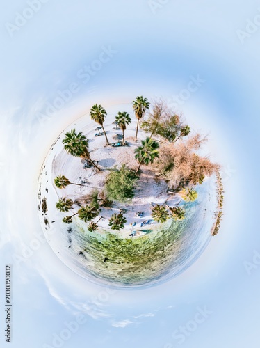 Tiny planet with tropical beach and palm tree. Surreal vacation spot on remote island. Conceptual landscape representing travel, relaxation and summer holiday getaway in alien world.